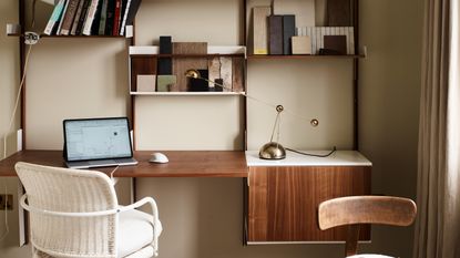 A built-in home office desk in dark wood with a white rattan desk chair