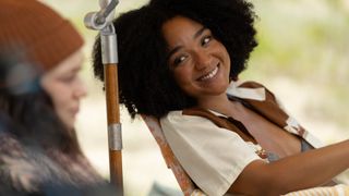 Aisha Dee as Chanelle lounging a deckchair smiling next to Milla.