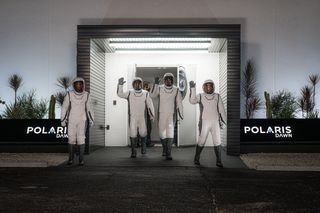 four people in white space suits wave in a parking lot