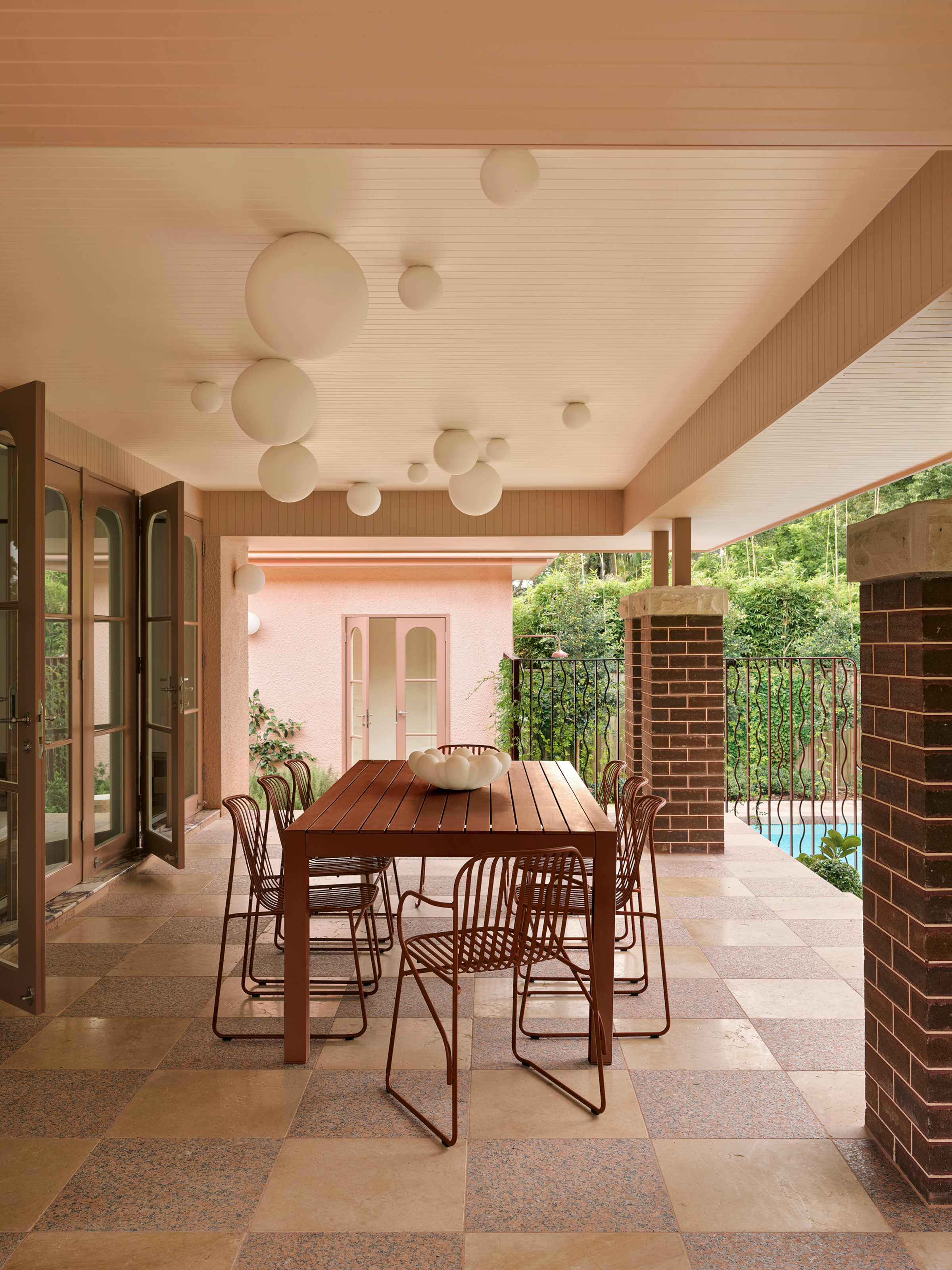 Outdoor dining space under cover with globe ceiling lights, checkerboard tiles and rust table