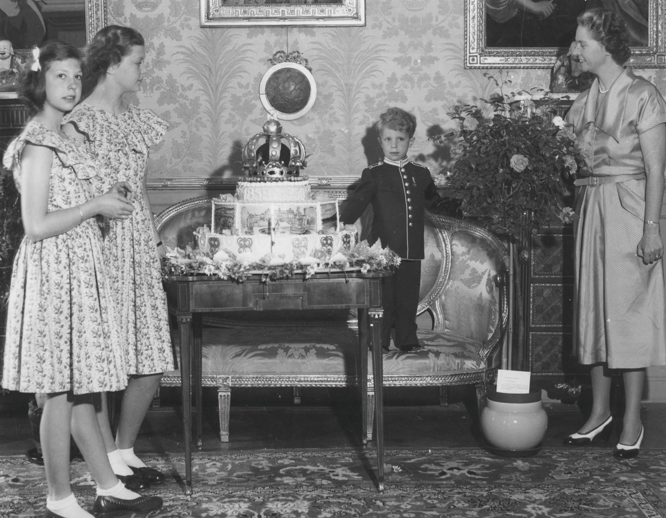 King Carl Gustaf standing on a sofa in front of a cake as a child with his mother and two of his sisters watching
