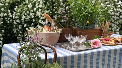 outdoor table set with glasses, food and a striped blue and white tablecloth