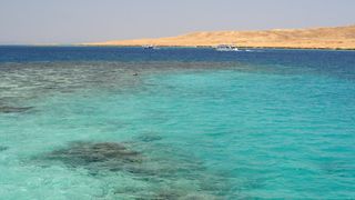 Landscapes of the Red Sea in Egypt with clear blue waters in the foreground and sandy yellow low lying areas in the distance.