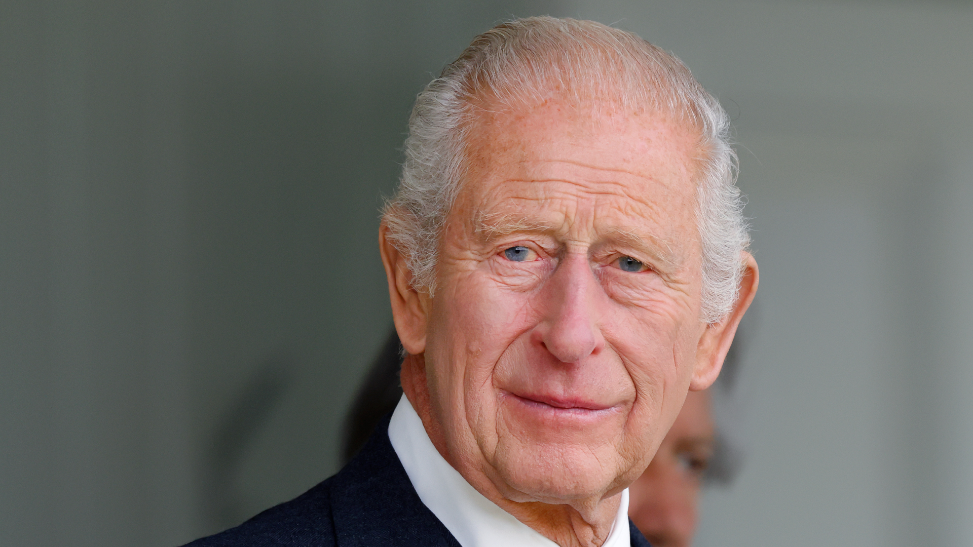 A headshot of King Charles wearing a suit and tie