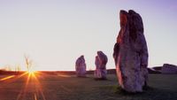 A series of stone pillars are seen in the setting sun overlooking a field