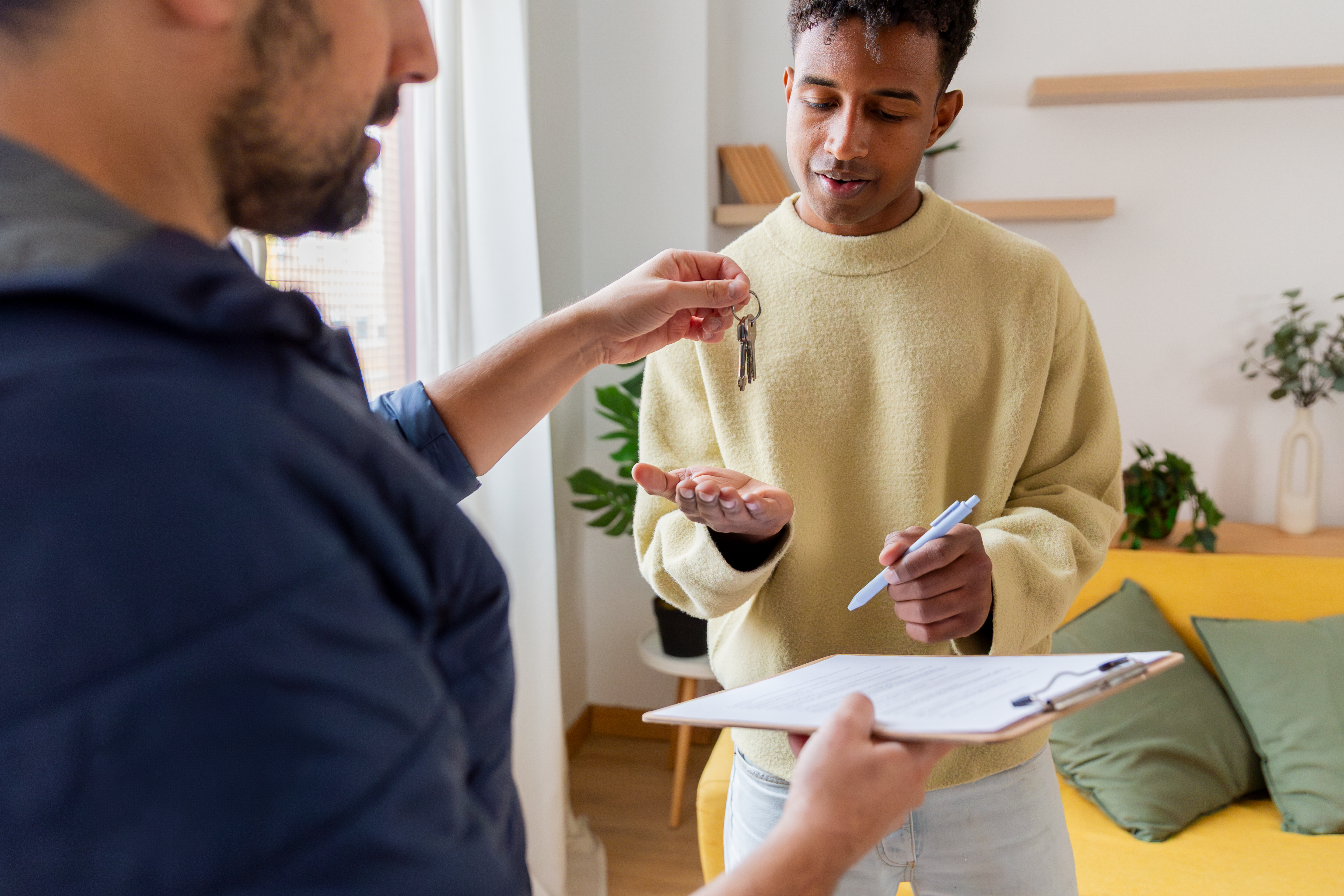 Landlord gives tenant the key to a property as he signs document on a clipboard.