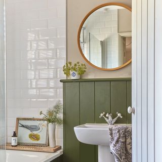 bathroom with white metro tiles around bath and green panelling on wall with round brass mirror