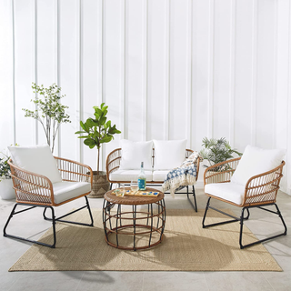 A wicker and metal outdoor and indoor furniture set on a jute rug with plants surrounding it. 