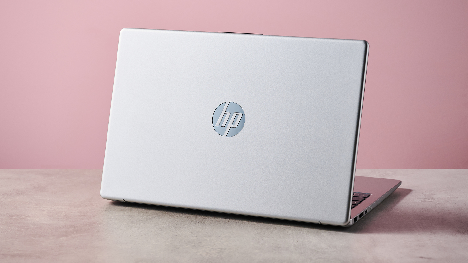 Rear three-quarter view of HP Laptop 14 open on white desk with pink wall in background