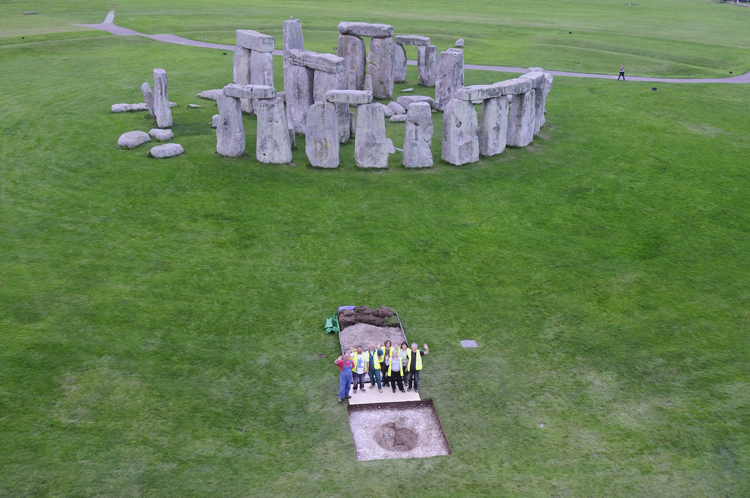  An aerial view of Stonehenge with a group of archaeologists standing in the foreground near an excavation site.