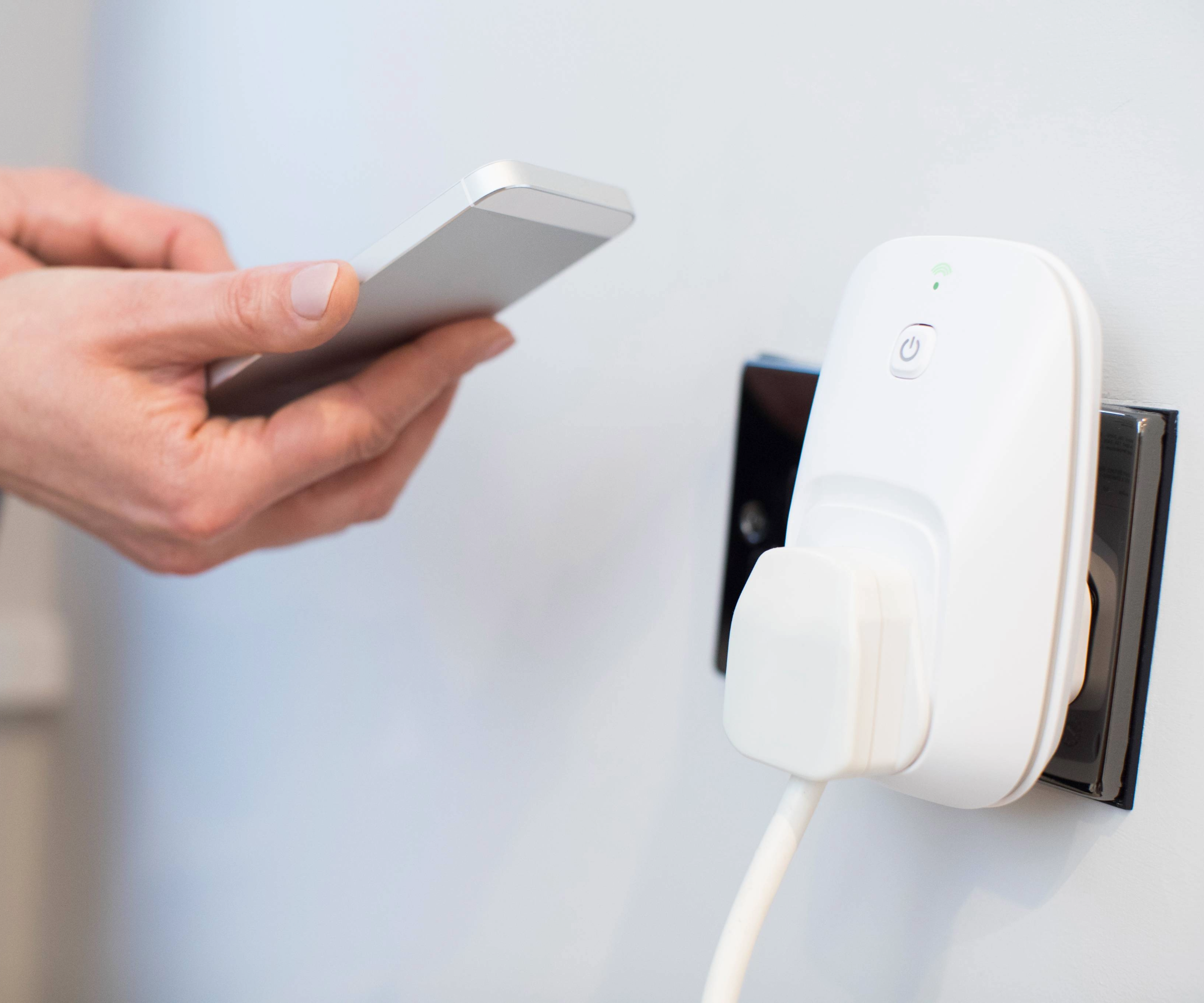 Smart plug in a socket with a hand holding a phone next to it
