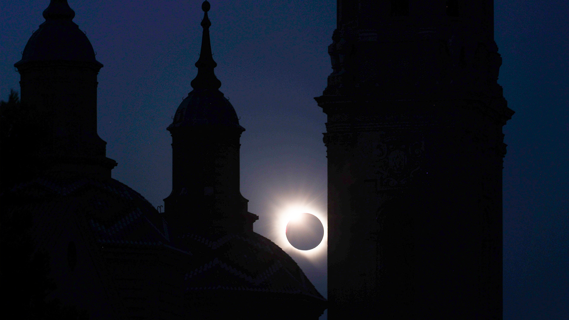 A silhouetted cathedral (Catedral-Basilica de Nuestra Senora del Pilar) with the total solar eclipse positioned in between the buildings.
