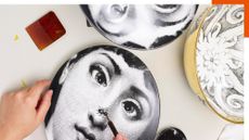 Close-up image of dinner plates with black and white faces on them. They are on a white table and there is a hand in the bottom left corner holding the plate