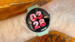 Close-up of the Google Pixel Watch 5 with an AI-generated watch face with the time and sate shown as if they are made of deli meats