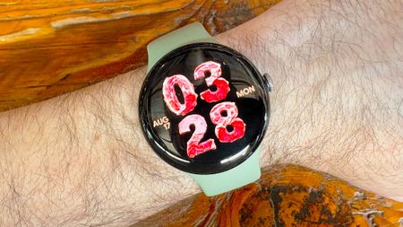 Close-up of the Google Pixel Watch 5 with an AI-generated watch face with the time and sate shown as if they are made of deli meats