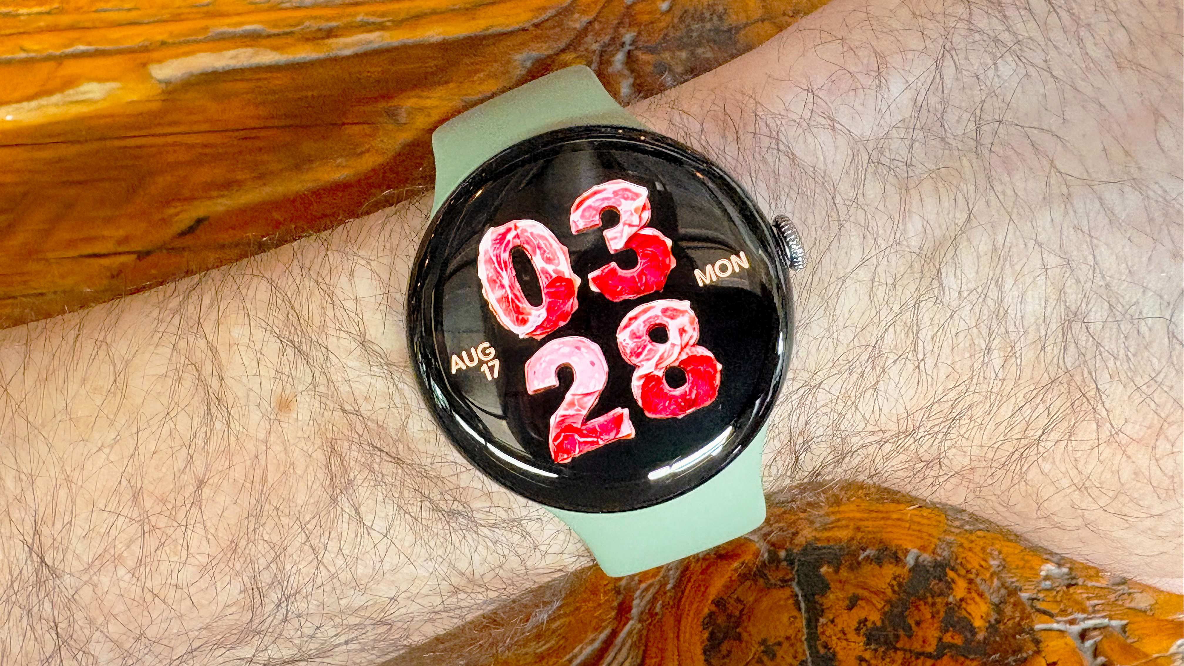 Close-up of the Google Pixel Watch 5 with an AI-generated watch face with the time and sate shown as if they are made of deli meats
