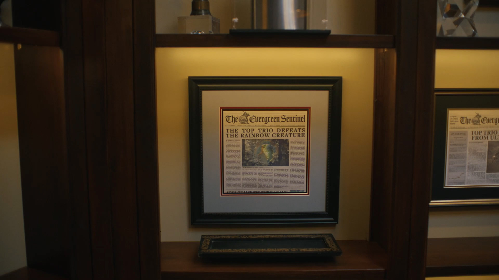A framed newspaper clipping of the Top Trio defeating Rainbow Creature in Peacemaker season 2 episode 1
