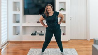 Woman standing on rug in living room in workout clothes