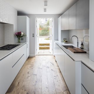 White narrow kitchen with wood flooring