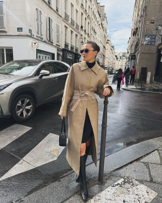 Fashion influencer @cocoschiffer in Paris wears an anti-trend outfit that is designed with a layer, a turtleneck sweater, a black skirt and knee-high boots.