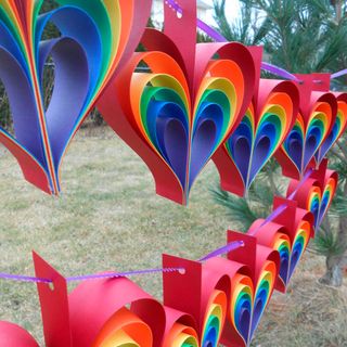 rainbow heart shapped bunting strung up on purple ribbon, in a yard with grass