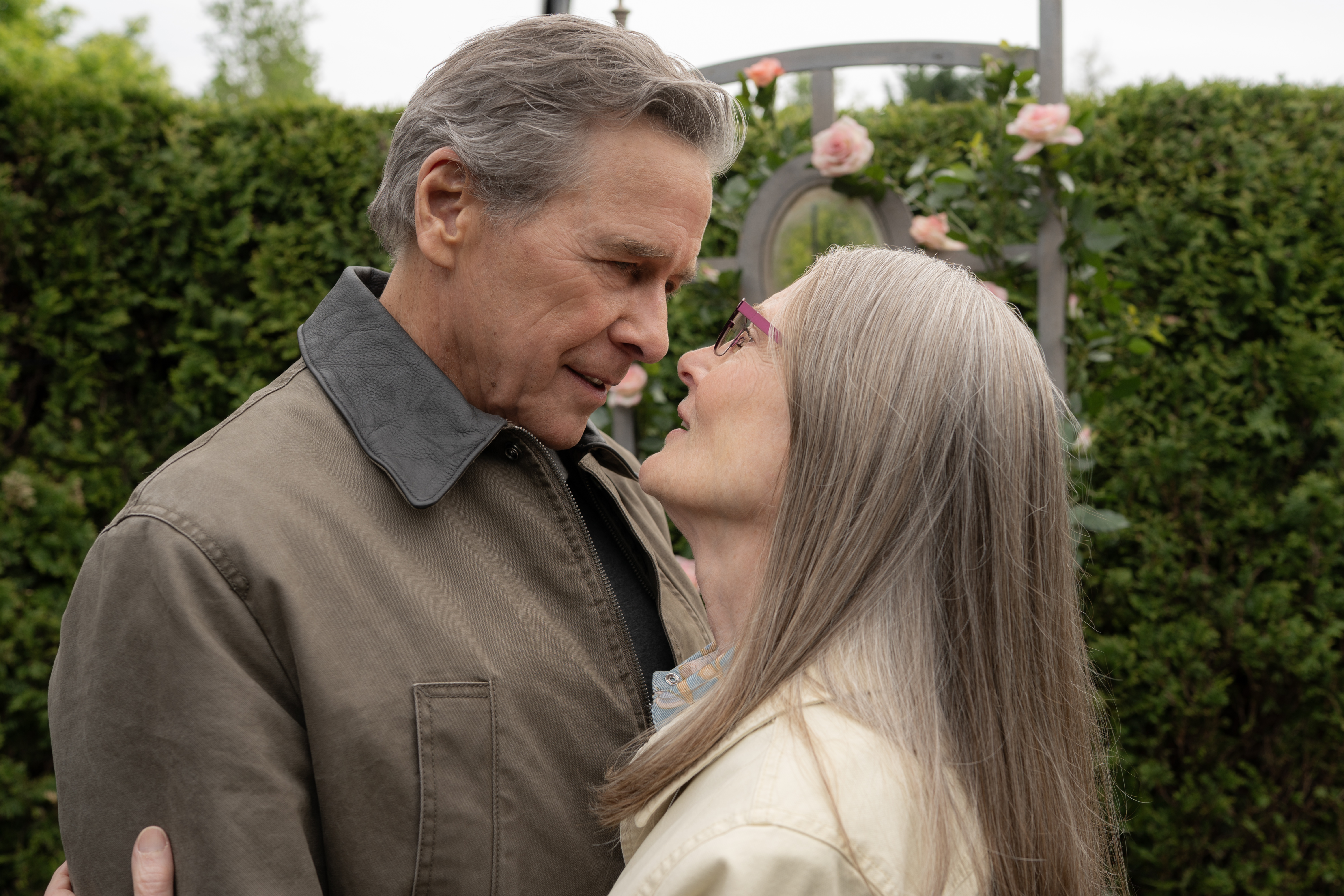 Tim Matheson as Dr. Vernon Doc Mullins and Annette O'Toole as Hope McCrea embrace outdoors in a garden in a still from virgin river season 7