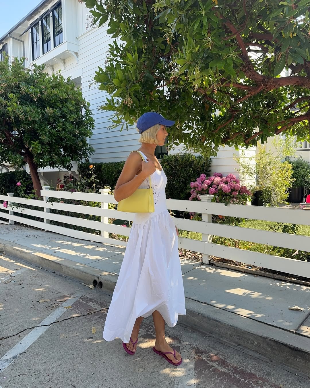 A woman wearing a white dress, baseball cap, and flip flops.