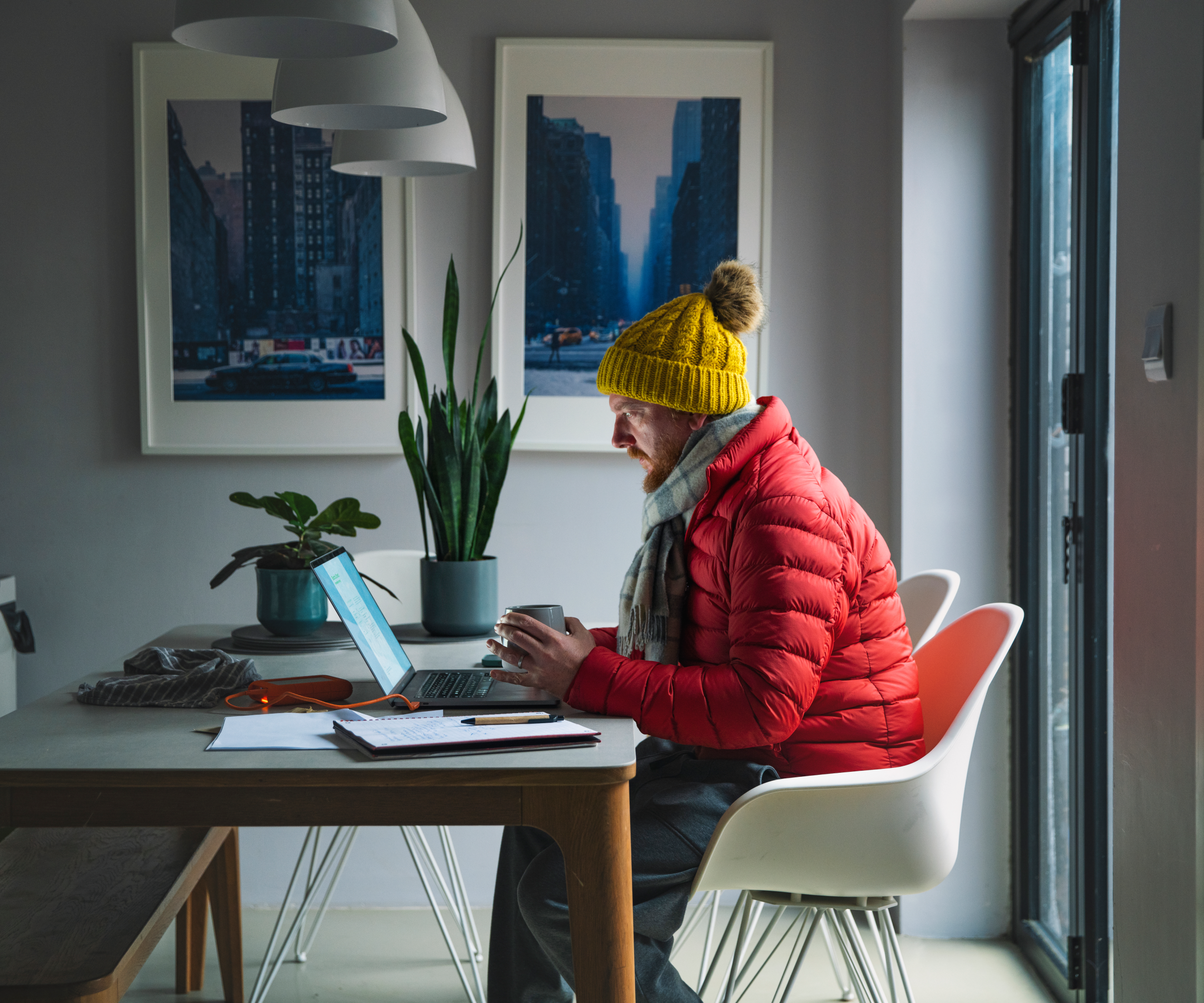 man working on laptop sat at table wearing puffer jacket, hat and scarf
