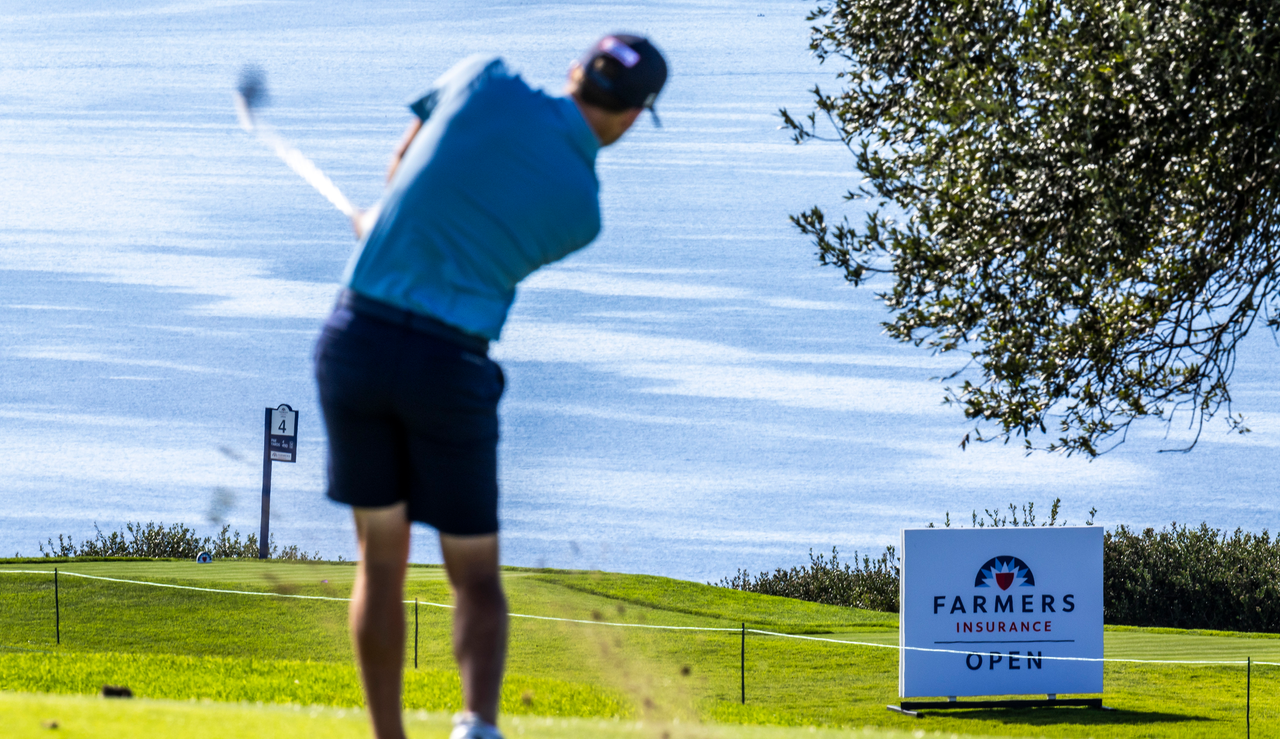 A golfer hits a shot in front of a Farmers Insurance Open sign