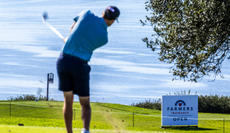 A golfer hits a shot in front of a Farmers Insurance Open sign