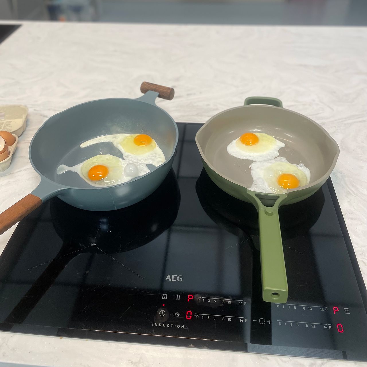 Two frying pans each containing two fried eggs on an induction hob on a white worktop