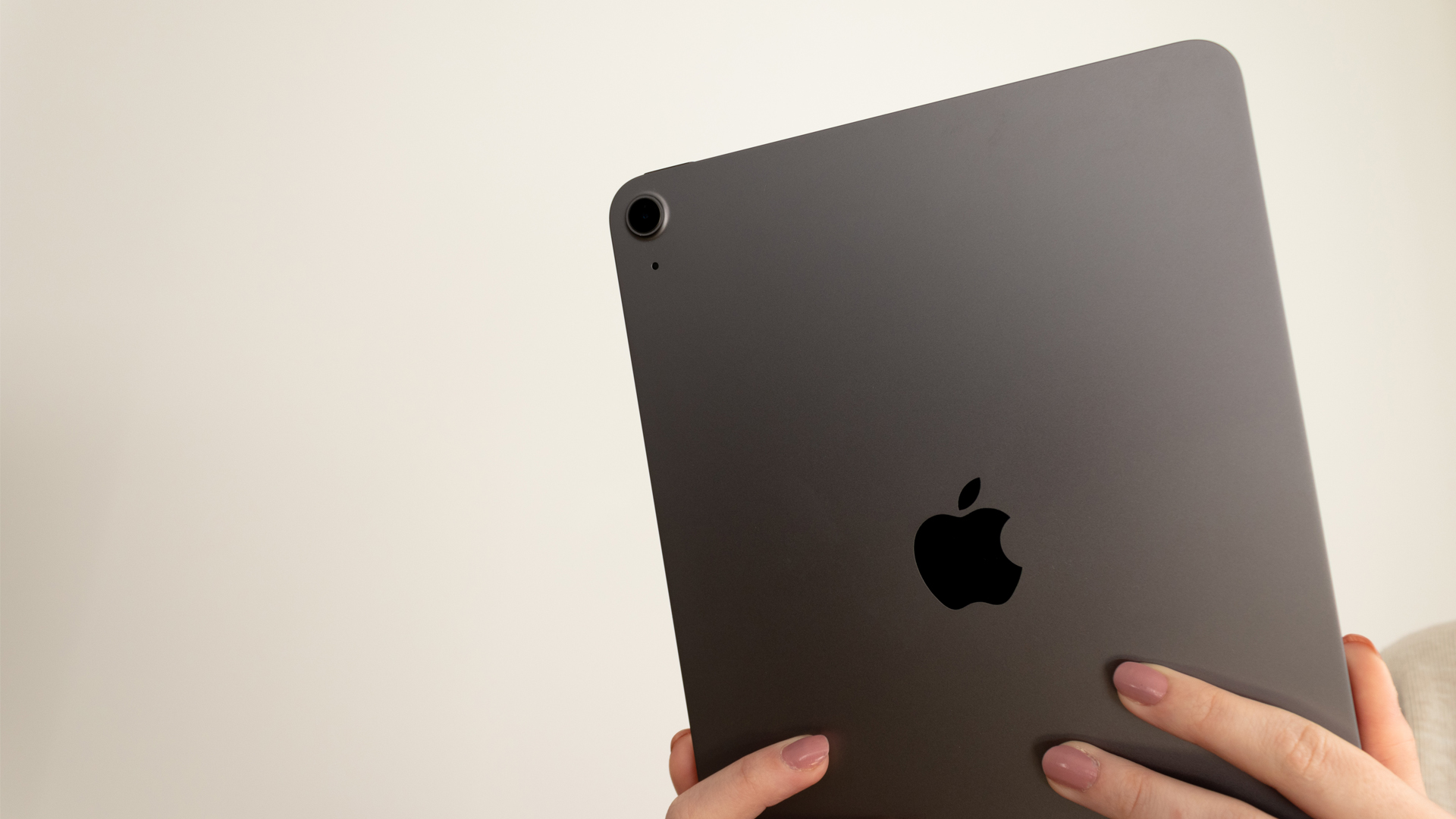 A photograph of the rear of an Apple iPad Air being held up in front of a wall