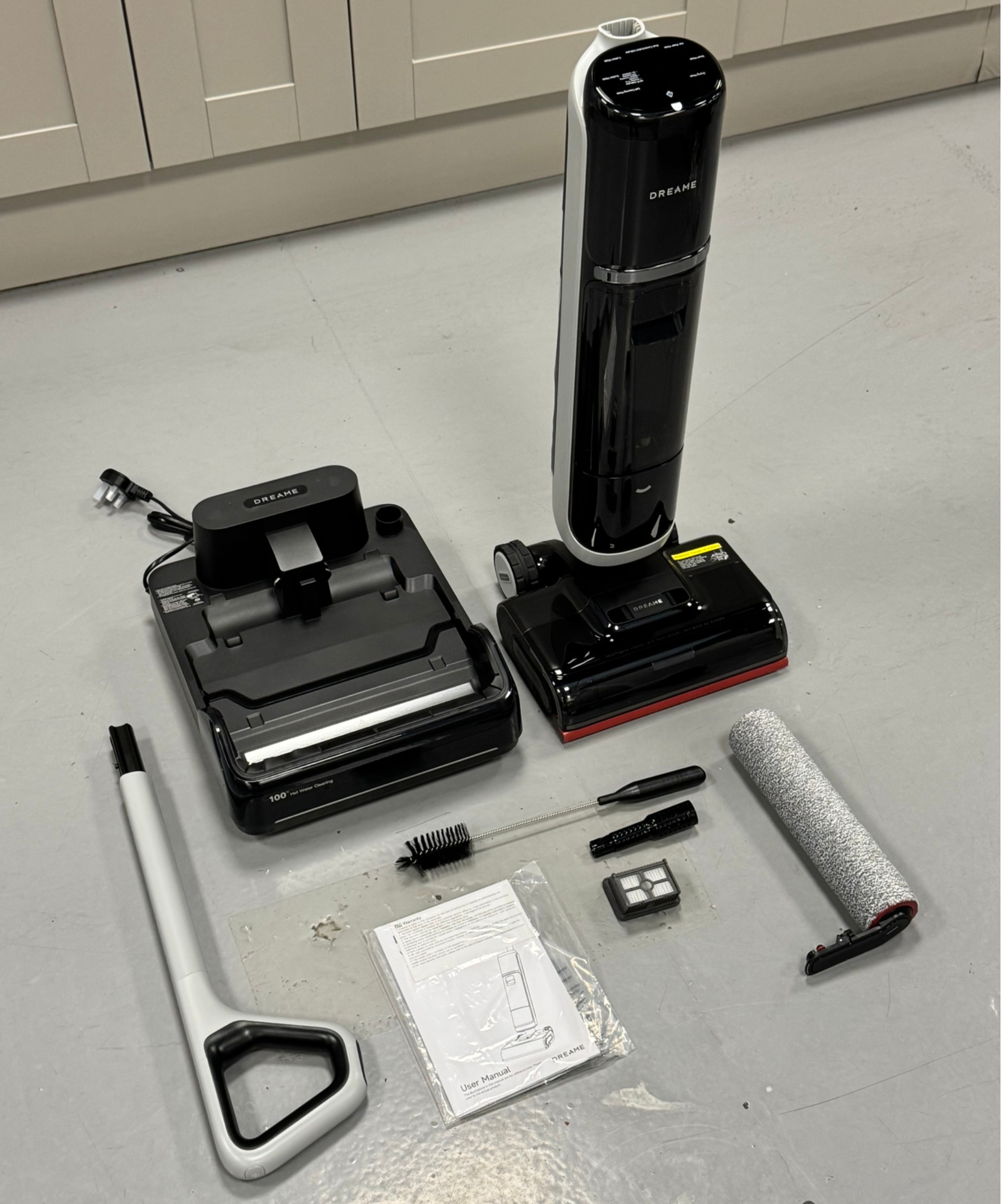 Everything included with the Dreame H15 Pro Heat vacuum-mop combo. Vacuum, charging base, handle, cleaning brush, roller, filter, and instruction manual are laid out on gray floor.