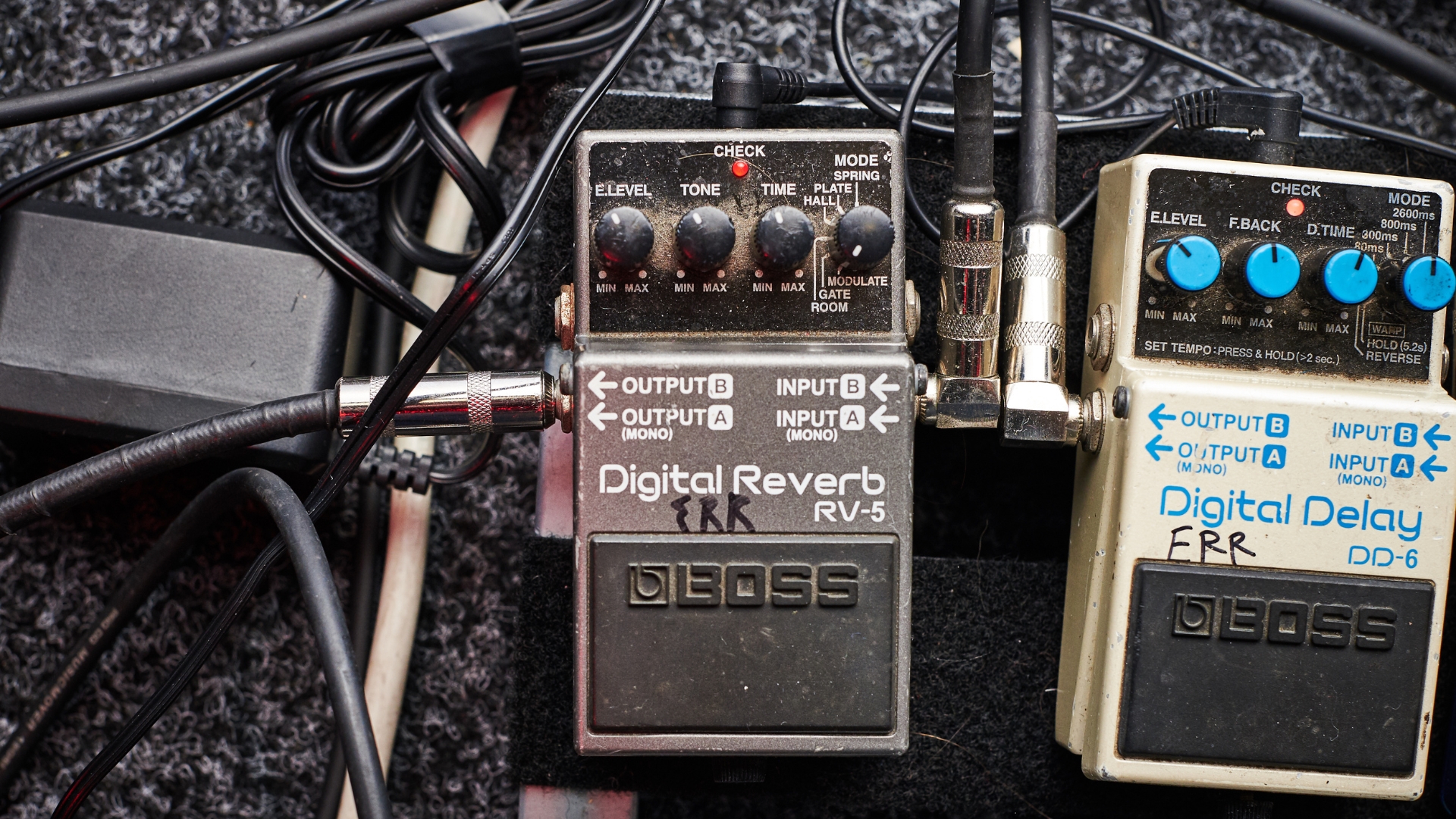 Two Boss pedals on a messy pedalboard with a patch cable connecting them