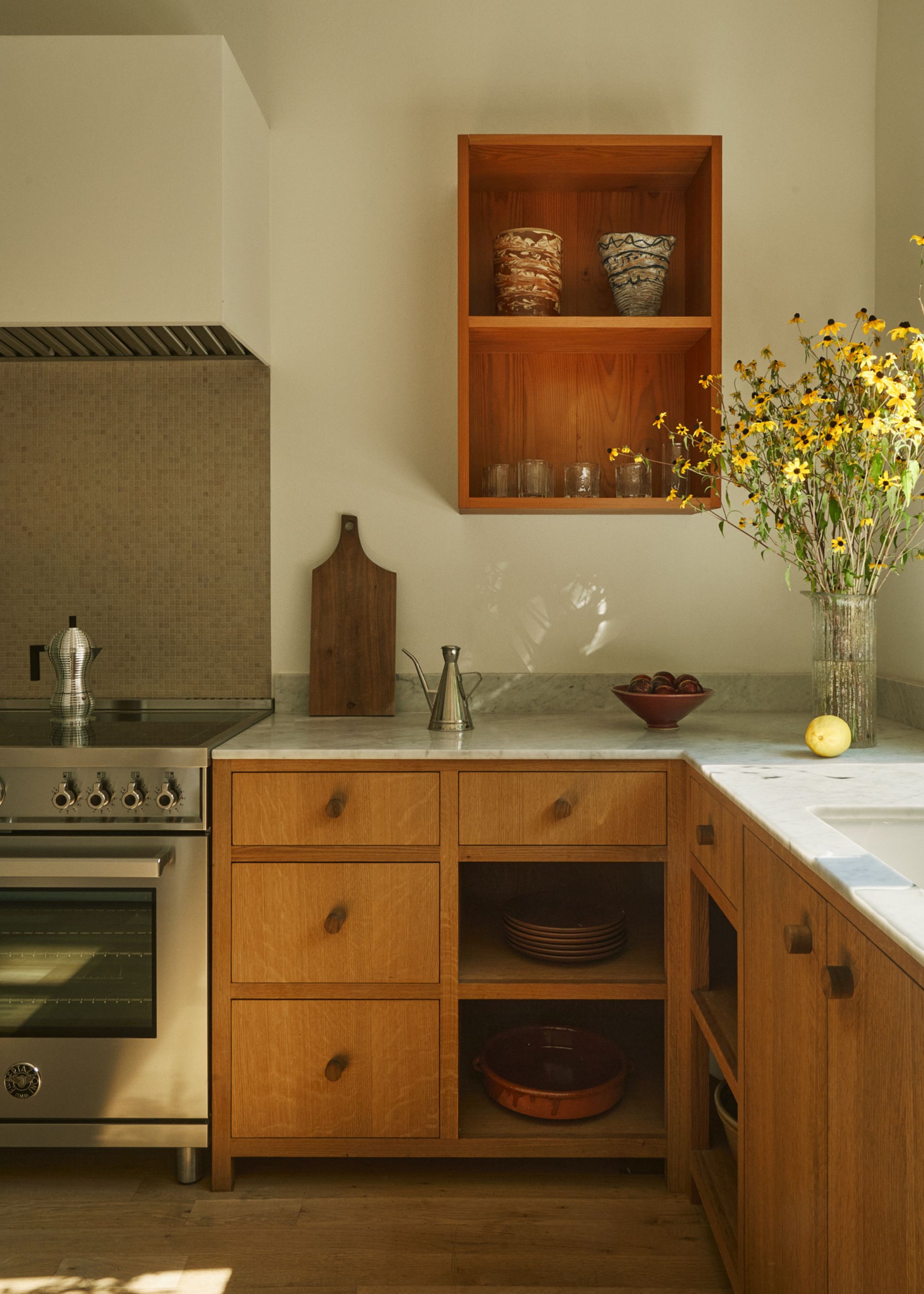 A kitchen with an open corner shelf with dishes and kitchen essentials. There is also a view of the countertop, stove as well as oven
