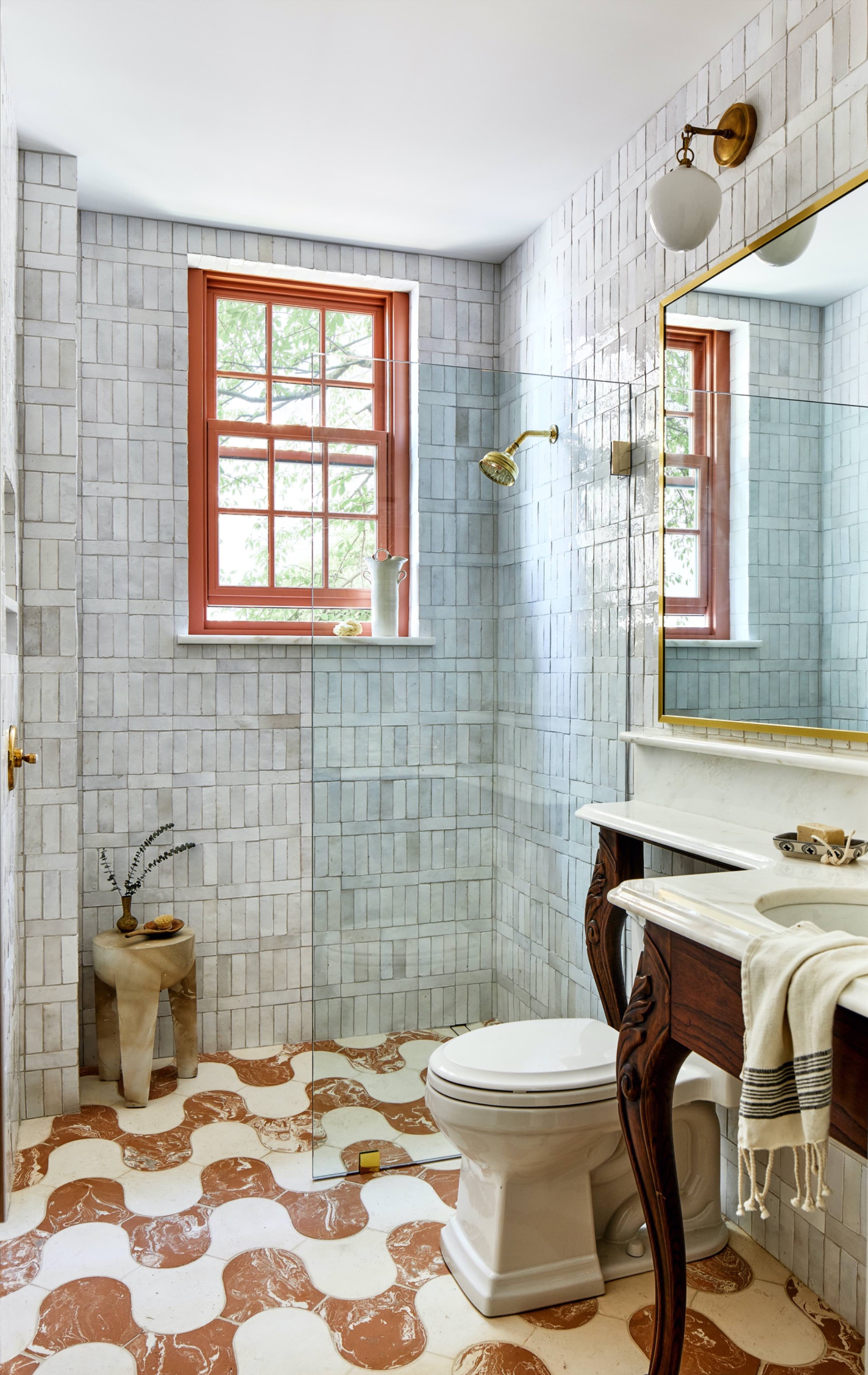Small bathroom with pale blue wall tiles, a curving terracotta-and-white tiled floor, vintage-style vanity and frameless shower screen.