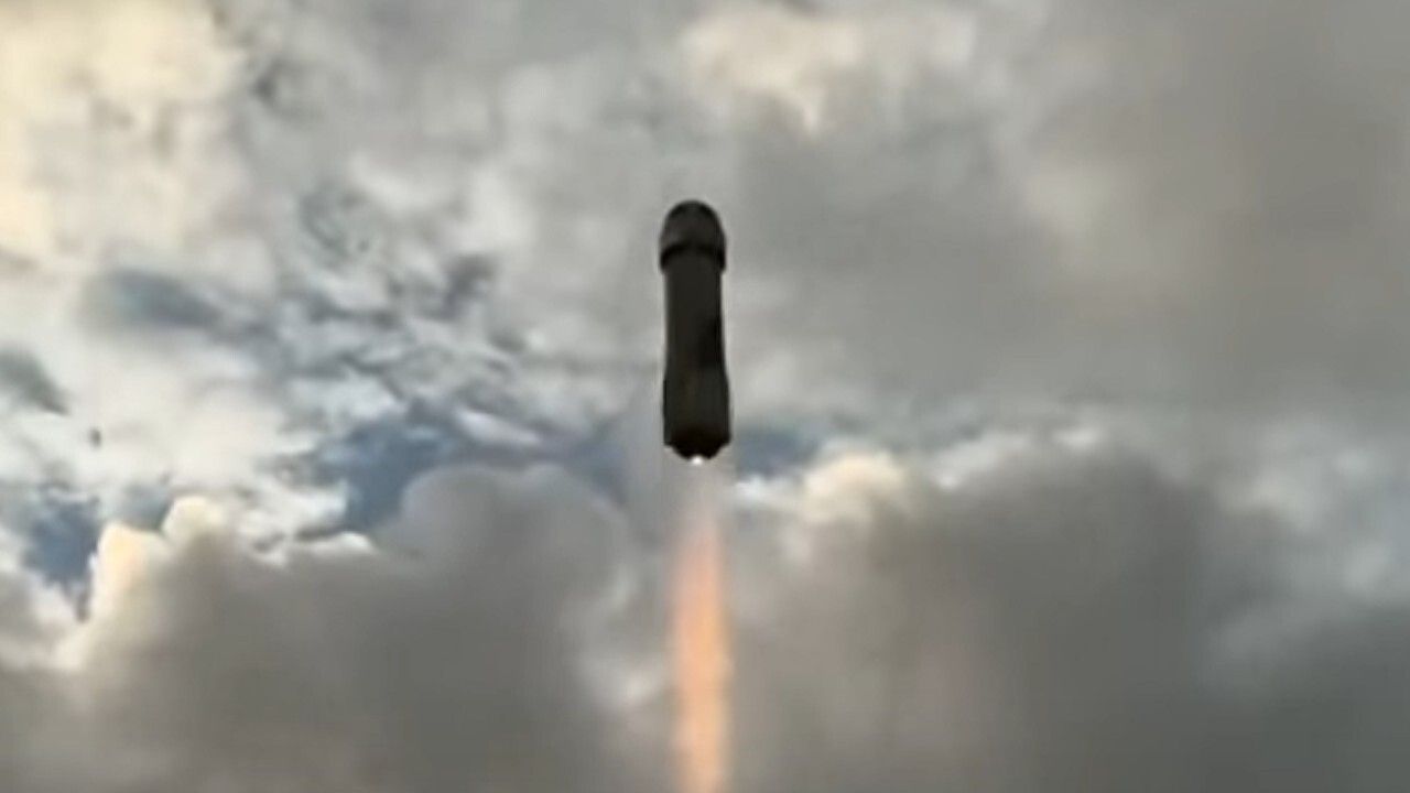 A Blue Origin New Shepard rocket is silhouetted against a cloudy sky during a NS-36 space tourist launch.