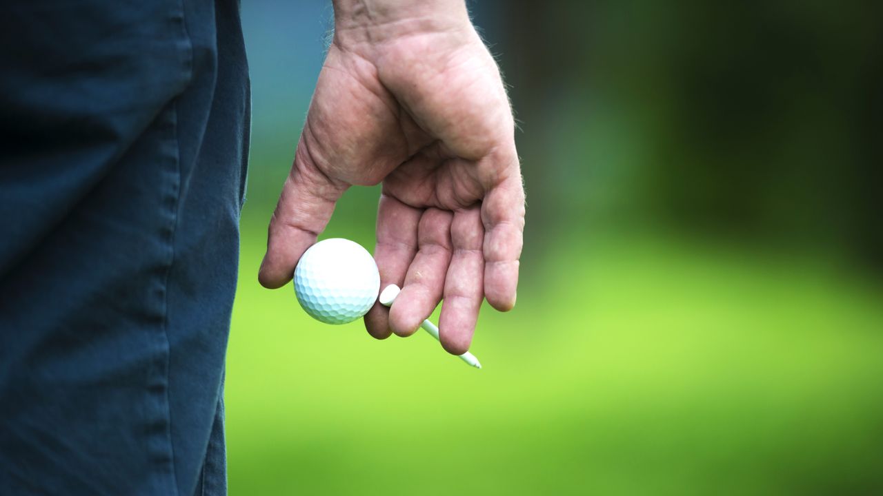 The honour in golf: A golfer&#039;s hand holding a ball and a tee