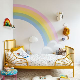 kids bedroom with rainbow paint on wall and yellow bed