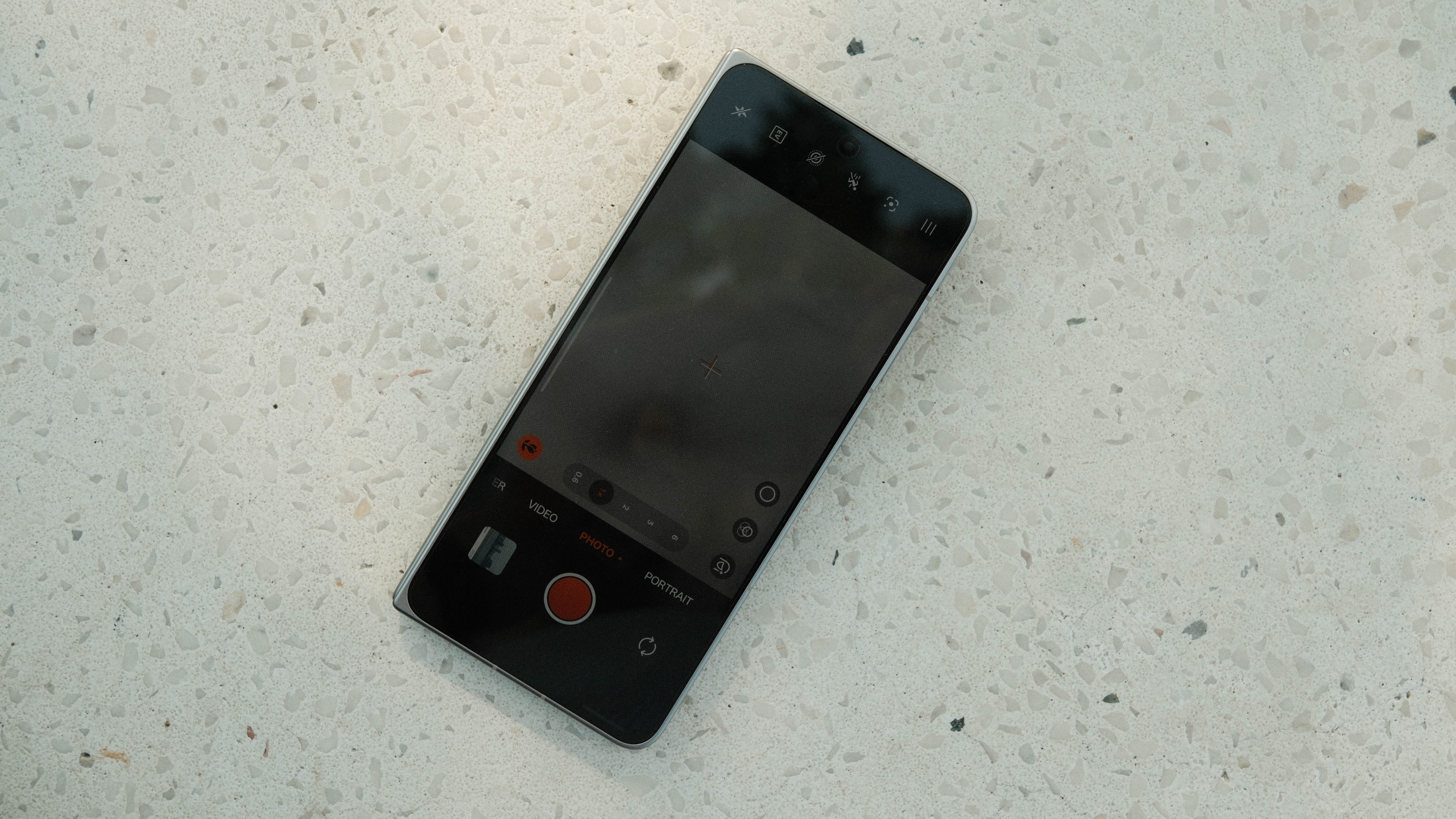 A top-down view of the phone's cover display showing the camera app interface. The screen is dark, showing various photography modes like "PHOTO," "VIDEO," and "PORTRAIT" at the bottom.