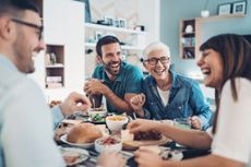 A group of adults is laughing over a meal. They all have great teeth.