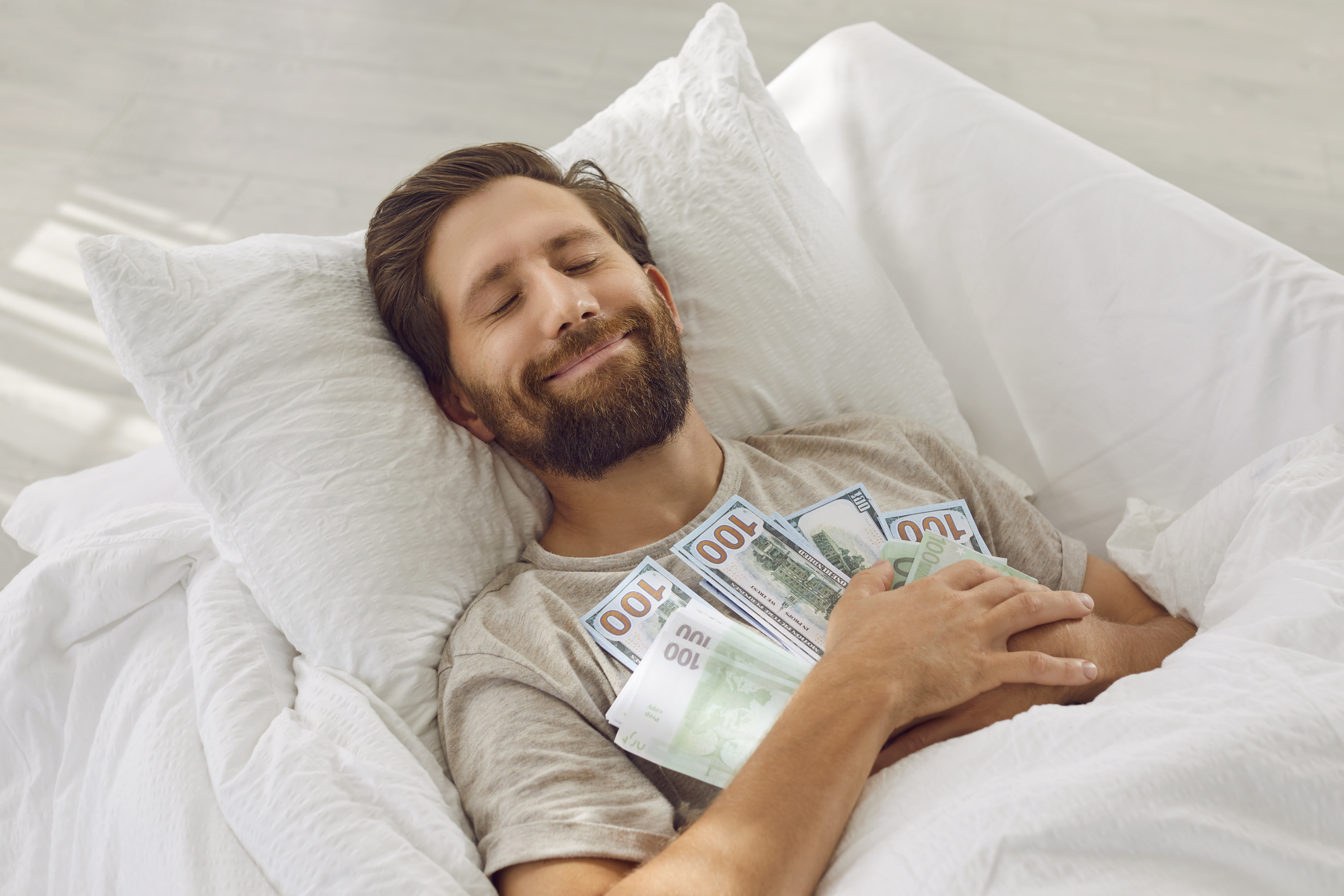 Man sleeping in a bed holding a lot of money 