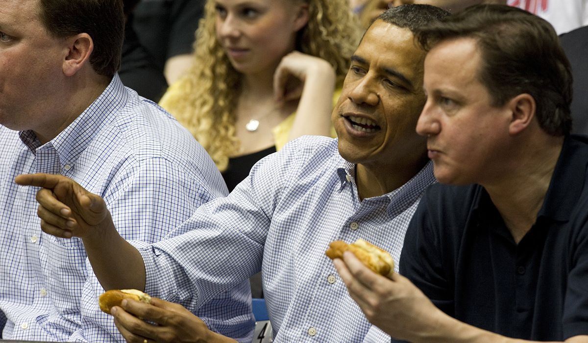 US President Barack Obama (C) talks with British Prime Minister David Cameron (R) as they eat hot dogs while sitting in the stands at University of Dayton Arena in Dayton, Ohio, March 13, 201