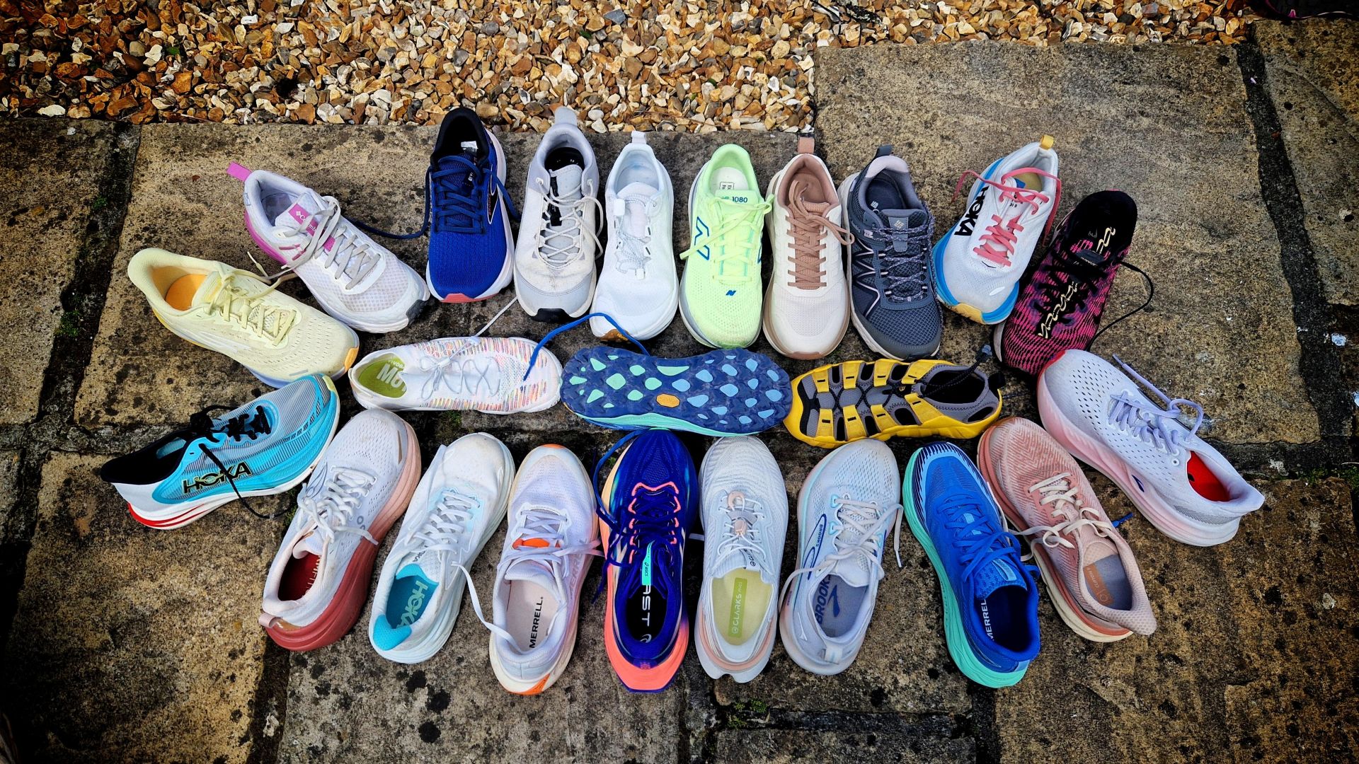 An aerial layout image of a collection of 23 single shoes displayed on stone tiles