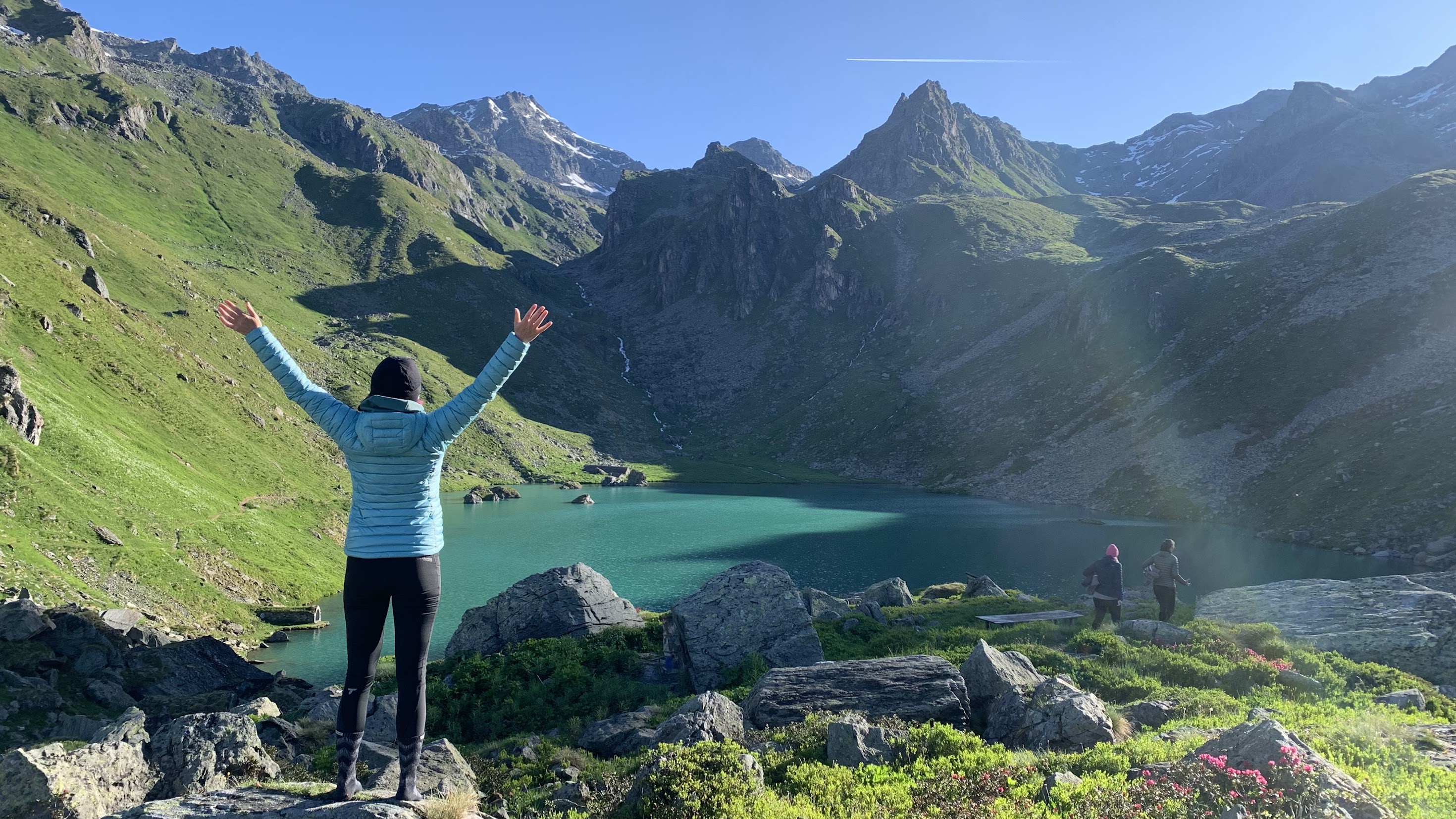 A woman hiker in one of the best down jackets for women throwing her arms in the looking at an alpine lake in Switzerland