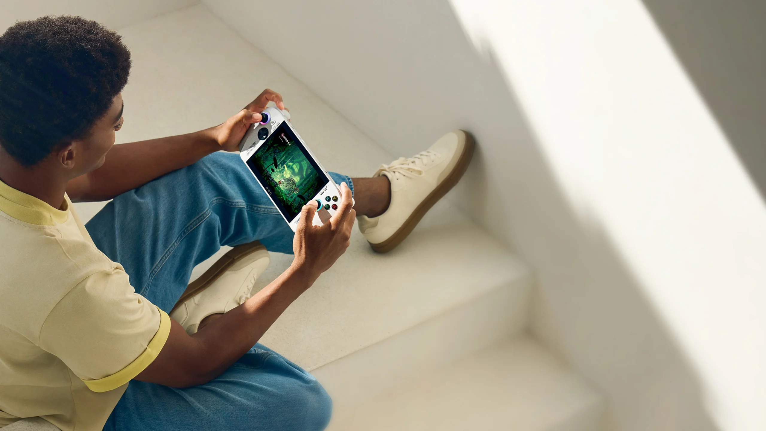 a man sitting on some stairs holding the Asus ROG Xbox Ally in his hands