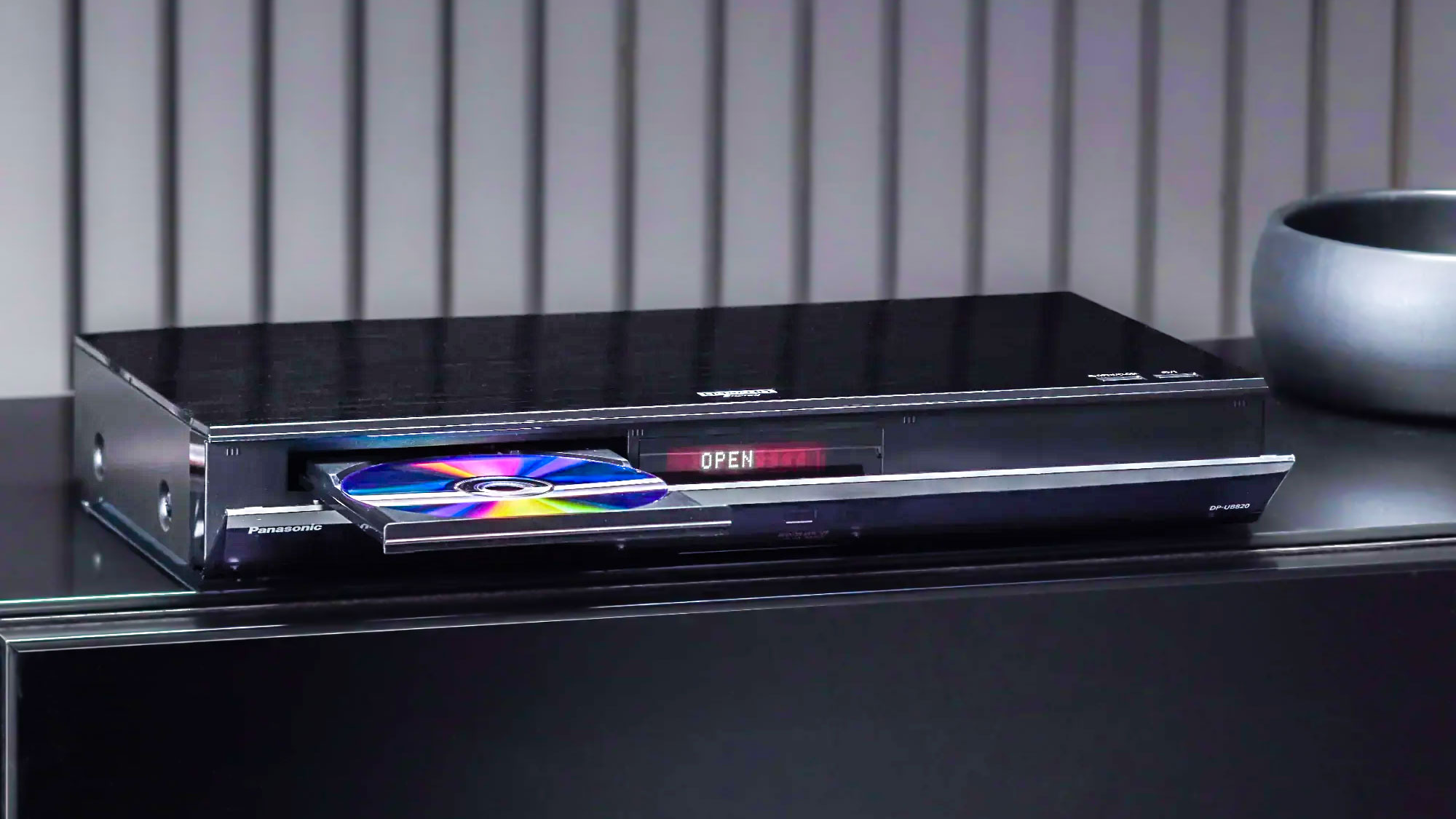 The Panasonic DP-UB8204K UHD Blu-ray player atop a credenza with its disc tray open
