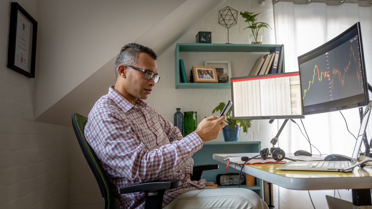 Person looking at phone while investing on computer