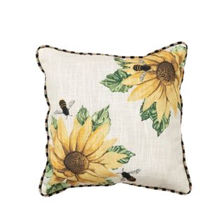 A beige cushion with an illustration of two sunflowers with a bee and a yellow and black striped border in the upper right and lower left corners.
