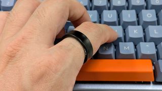 Close-up photo of the Samsung Galaxy Ring worn on the index finger of hand which is typing on a keyboard.